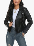 A woman wearing a black faux-leather moto jacket over a white t-shirt and distressed blue jeans, shown from the chest down against a plain white background.