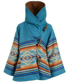 A women's wrap-style cape coat featuring a solid turquoise blue upper section and a Southwestern geometric patterned lower section in blue, orange, beige, and white. It has a high collar, a wrap-around front closure with brown toggle details, and wide sleeves, shown against a plain white background.