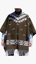 A brown woven poncho with white geometric patterns and fringe, worn over a light blue shirt and black turtleneck.