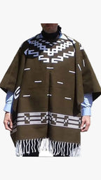 A brown woven poncho with white geometric patterns and fringe, worn over a light blue shirt and black turtleneck.
