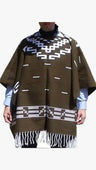 A brown woven poncho with white geometric patterns and fringe, worn over a light blue shirt and black turtleneck.