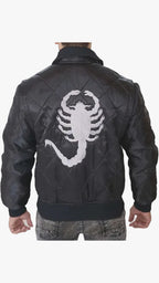 A man viewed from behind wearing a black quilted leather bomber jacket with a large white embroidered scorpion graphic on the back, paired with gray jeans against a light gray studio background.