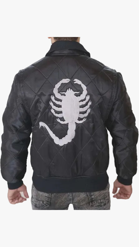 A man viewed from behind wearing a black quilted leather bomber jacket with a large white embroidered scorpion graphic on the back, paired with gray jeans against a light gray studio background.
