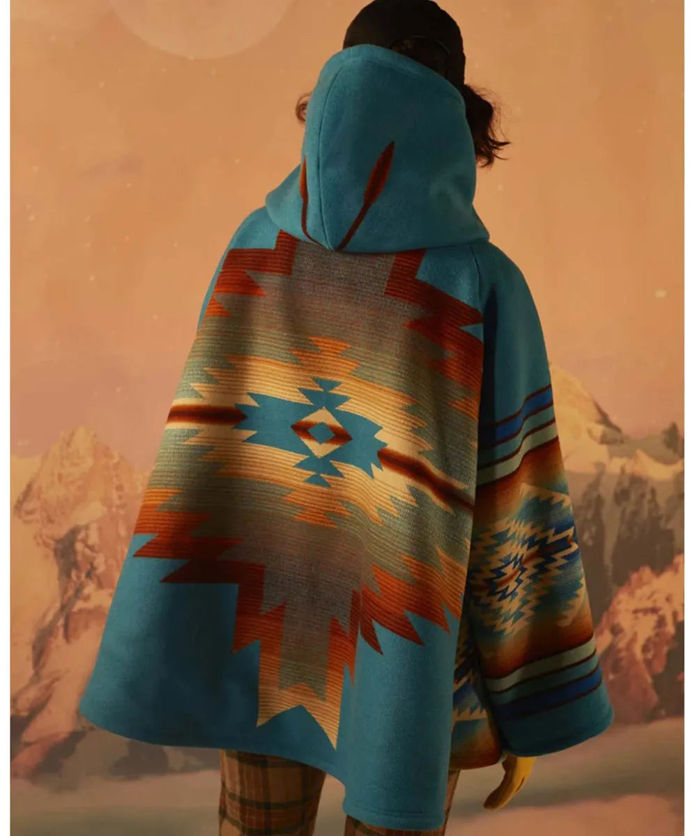 A person shown from behind wearing a hooded poncho with a Southwestern geometric pattern in turquoise, orange, red, beige, and brown, set against a warm-toned mountain landscape.